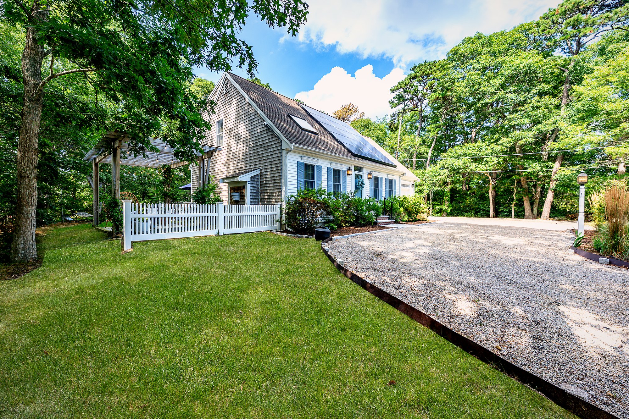 Cape-style front of Orleans Holiday House with the pergola, picket fence and gravel driveway